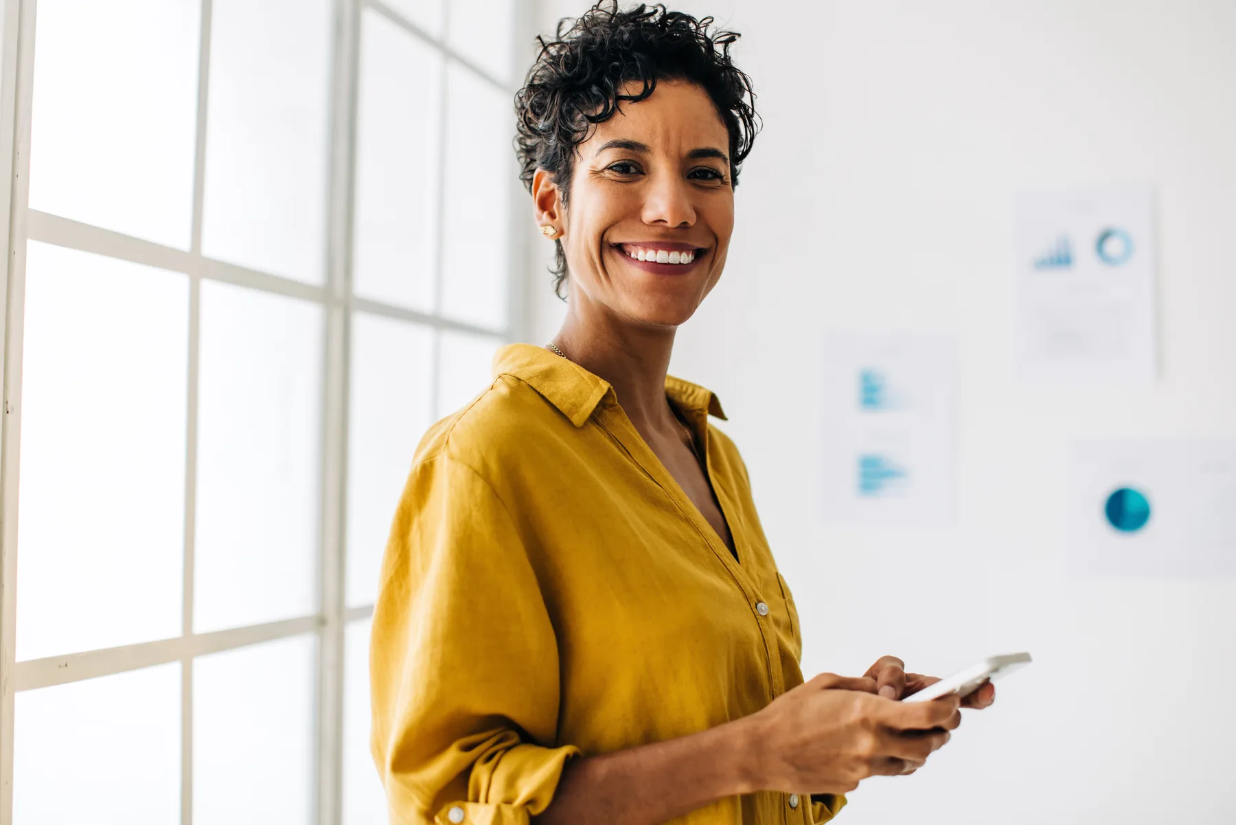 Smiling woman holding a phone in a yellow sweater